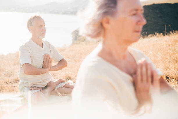 yoga Couple of senior people doing yoga exercises at the mountain on the background. Feeling the harmony. Concept of calm and meditation. Way to peace and balance. The Impact of Yoga and Nature on Senior Health stock pictures, royalty-free photos & images